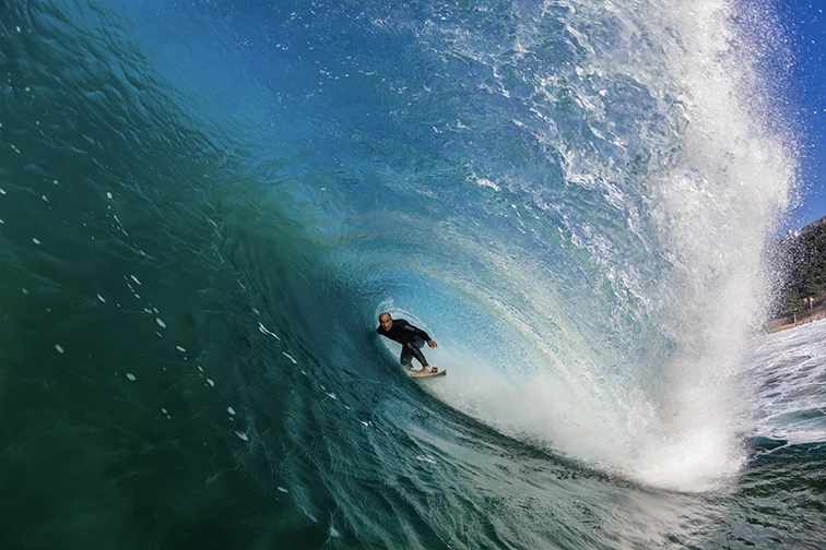 Surfer getting barrelled in wave on blue ocean